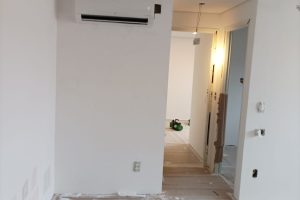 Sala em reforma com piso protegido, ferramentas, materiais de construção e ar-condicionado na parede.